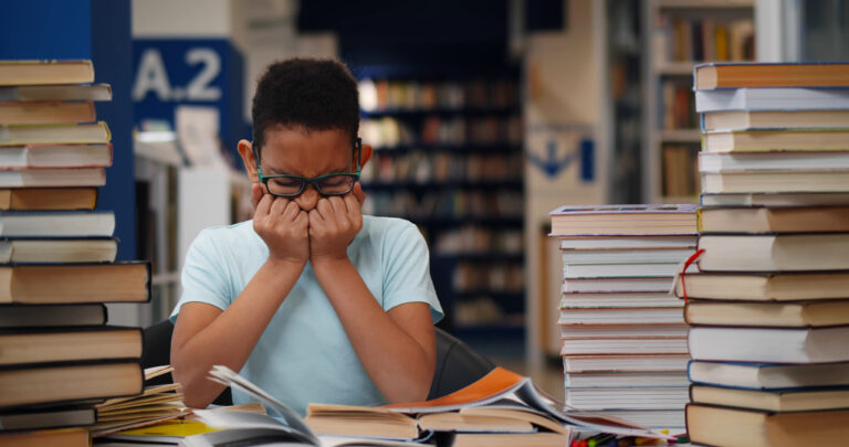 frustrated Child wearing glasses while surrounded by books at a desk