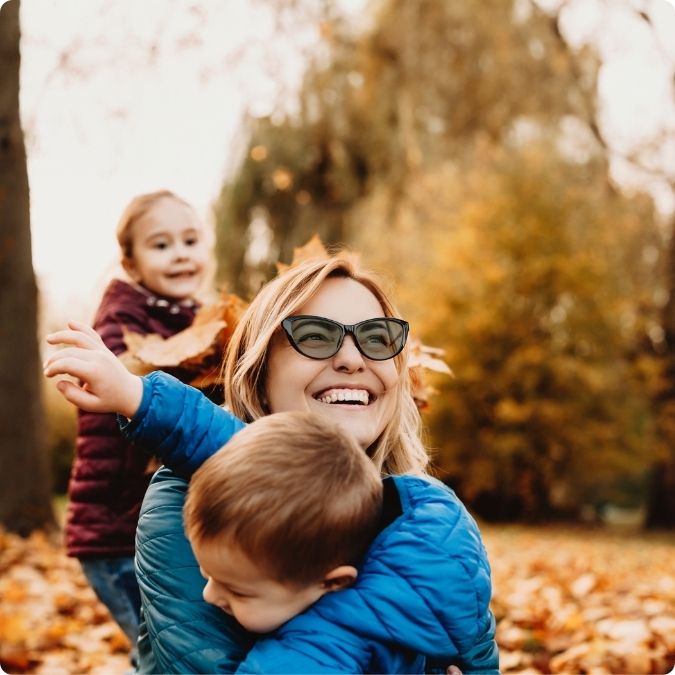 Smiling woman playing with children wearing Avulux migraine lenses outdoors without squinting