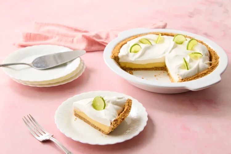 Slice of classic key lime pie topped with whipped cream and lime zest on a white plate